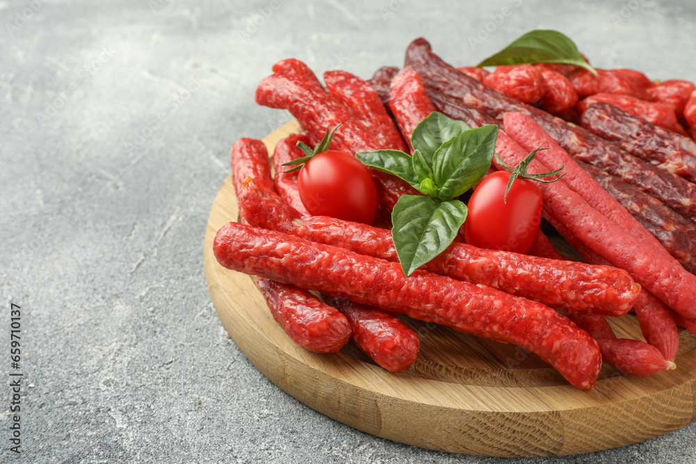 Different thin dry smoked sausages, basil and tomatoes on light grey table, closeup. Space for text Different thin dry smoked sausages, basil and tomatoes on light grey table, closeup. Space for text
