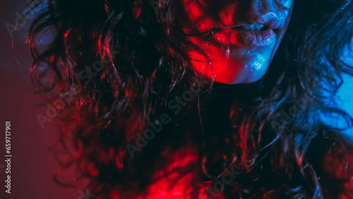 Club lifestyle. Sensual lady. Unrecognizable passionate brunette woman beautiful lips curly shiny hair radiant sweaty face skin in blue red light on dark background.