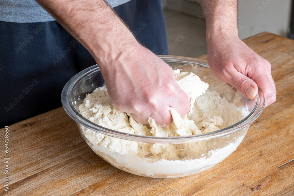 Fototapeta premium Man's hands kneading dough inside a glass bowl.