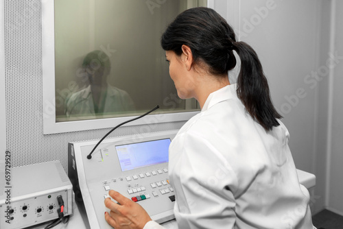 Audiologist woman doing the hearing exam to a mixed race manwoman patient using an audiometer in a special audio room.