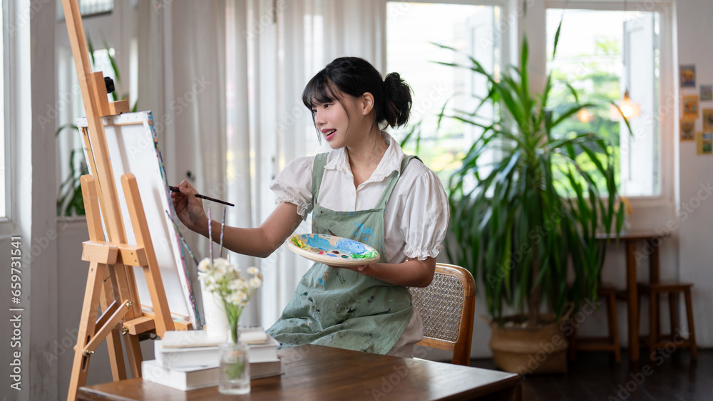 A beautiful Asian female artist painting on a canvas with water colors, working in her cosy studio. A beautiful Asian female artist painting on a canvas with water colors, working in her cosy studio.