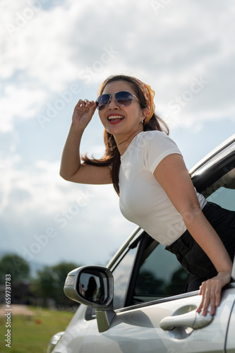 A happy Asian woman is enjoying the wind outside the car and having fun during her road trip.