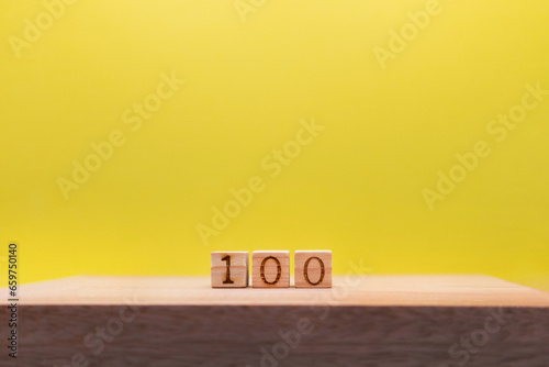 すき間をあけた100の数字のウッドキューブが奥にある黄色い背景