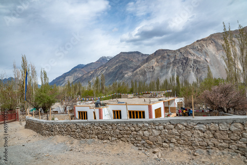 A scenic view of Himalayas and Ladakh ranges. Beautiful barren hills in Ladakh with dramatic clouds in the background.  View from the road from Nubra Valley to Turuk. Houses in valley. © Srijita Photography