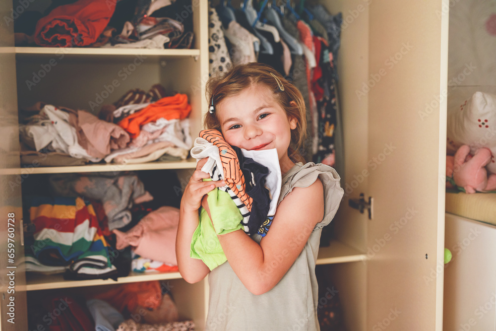 Little school girl standing by wardrobe with clothes. Preschool child putting shirts away and making decision for shirt to wear. Children get dressed in the morning for school. Little school girl standing by wardrobe with clothes. Preschool child putting shirts away and making decision for shirt to wear. Children get dressed in the morning for school.