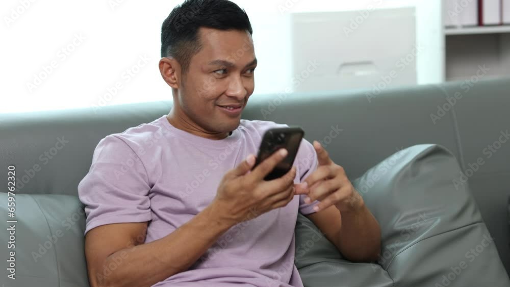 Cheerful middle-aged man sitting on sofa using smiley face on modern home phone, texting, scrolling, tapping technology. 4K Video Cheerful middle-aged man sitting on sofa using smiley face on modern home phone, texting, scrolling, tapping technology. 4K Video