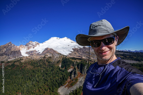 Adventurous athletic male hiker taking a selfie with the sun shinning and Mount Baker in the background. 