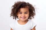Adorable Mexican toddler girl with afro hair smiles sweetly against white background, highlighting her innocence and charm.