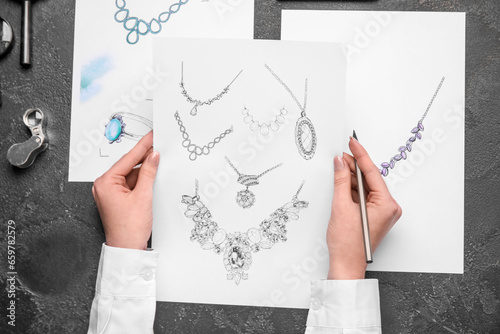 Female jeweler with drawings of adornment on dark table, top view photo