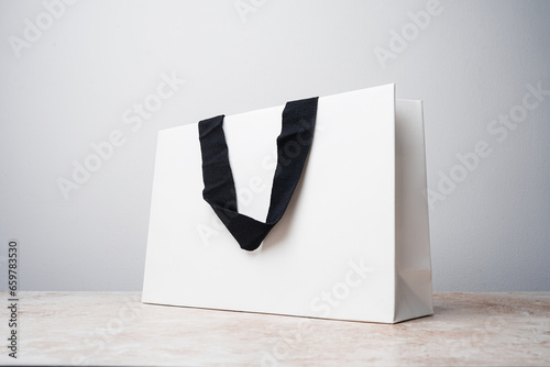 White paper bag with black fabric handles on a marble table, white background. Mockup, brand mock up
