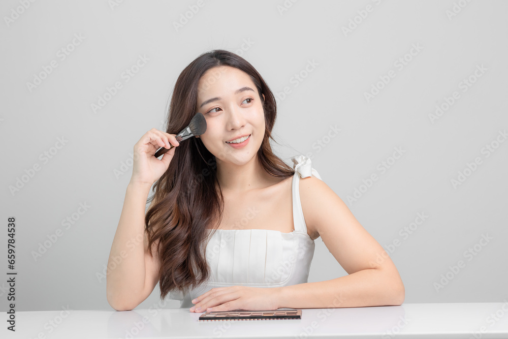 Beautiful young Asian woman with clean, white, healthy skin. Young Asian woman holding makeup brush and applying makeup at home. Beauty on face. Beautiful young Asian woman with clean, white, healthy skin. Young Asian woman holding makeup brush and applying makeup at home. Beauty on face.