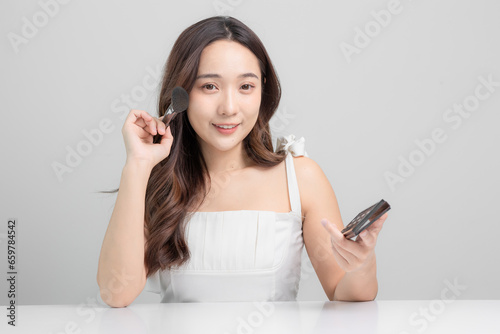 Beautiful young Asian woman with clean, white, healthy skin. Young Asian woman holding makeup brush and applying makeup at home. Beauty on face.