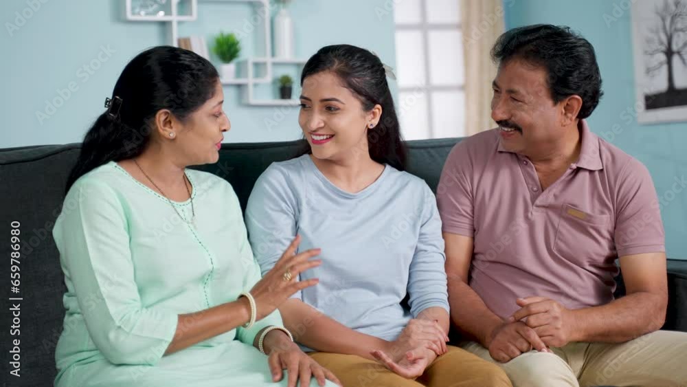 Happy smiling indian middle aged parents with daughter talking each other by looking at camera on sofa at home - concept of Parental Bonding, Family Conversation and Relaxed Discussion. Happy smiling indian middle aged parents with daughter talking each other by looking at camera on sofa at home - concept of Parental Bonding, Family Conversation and Relaxed Discussion.
