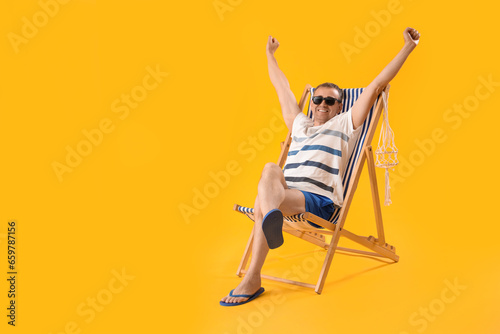 Leinwand Poster Mature man relaxing in deck chair on yellow background