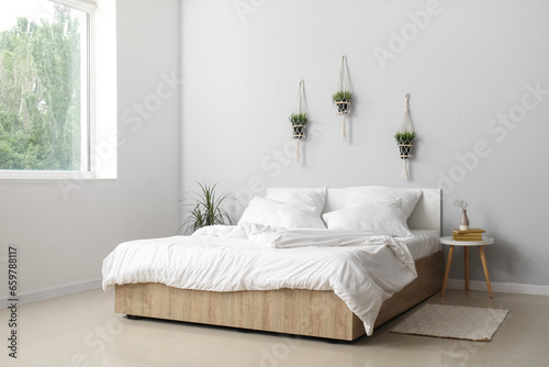 Interior of light bedroom with large double bed  white pillows and houseplants