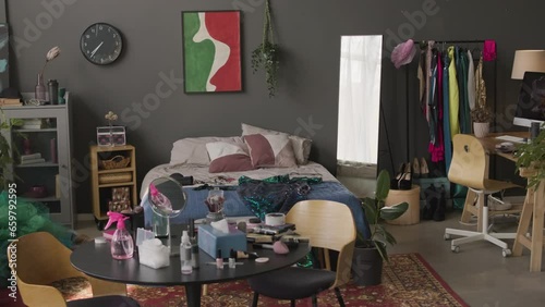 No people shot of messy anti minimalist creative apartment interior filled with lots of details and colors, makeup products on table and bright fancy dresses on rack photo