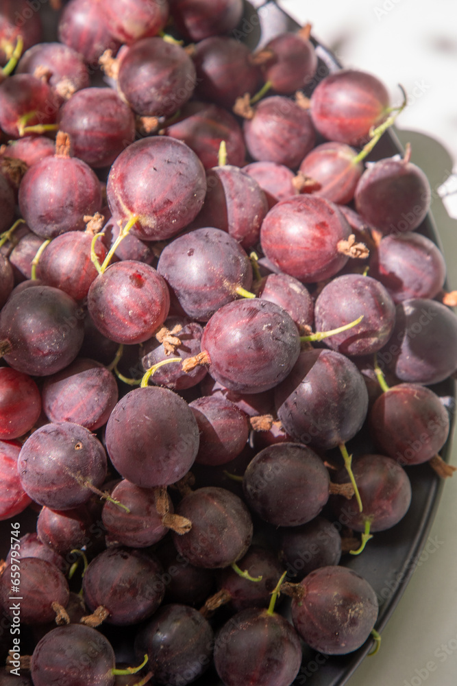 Gooseberries in a plate on the table. Vitamin summer food. Berry harvest top view. Pink berries on white background with shadow. Gooseberries in a plate on the table. Vitamin summer food. Berry harvest top view. Pink berries on white background with shadow.