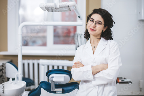 Professional young dentist posing confidently beside modern dental equipment in a dental clinic. Portrait of female doctor.