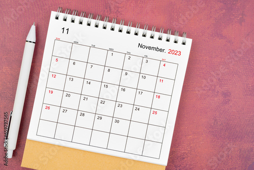 The November 2023 desk calendar and pen on red color background.