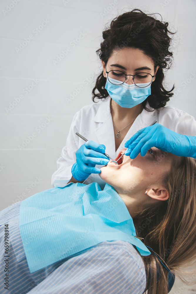 Female dentist examining patient's teeth on dentist chair, view from patient's side.