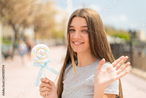 Teenager girl holding a lollipop saluting with hand with happy expression