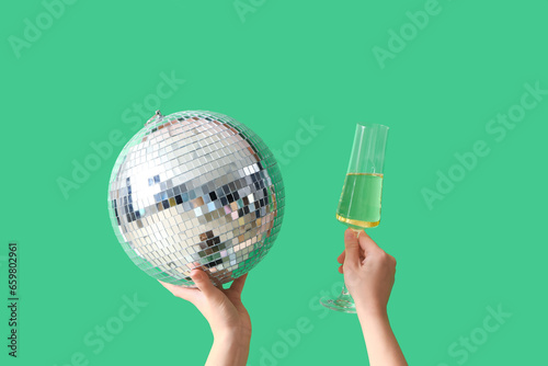 Female hands with glass of champagne and disco ball on green background. Birthday celebration