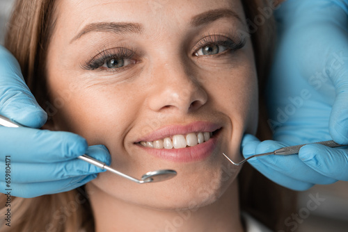 Beautiful and beautiful woman at dentist's appointment. Close-up face looking and smiling at camera. Dentist's hands with instruments near patient's smile and teeth. Dental Clinic Treatment and Care