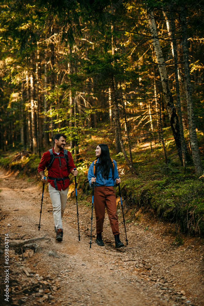 Fototapeta premium A multiethnic couple sets off on an invigorating hike, equipped with backpacks and walking poles to conquer the challenging yet rewarding trail