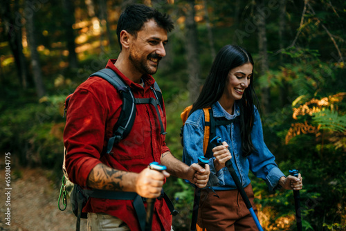 A multiethnic couple in love sets off on an invigorating hike, equipped with backpacks and walking poles to conquer the challenging yet rewarding trail © La Famiglia