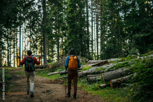 A multiethnic couple sets off on an invigorating hike, equipped with backpacks and walking poles to conquer the challenging yet rewarding trail