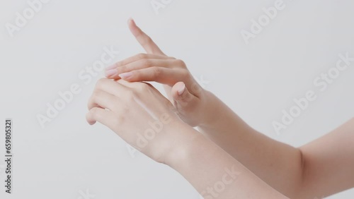 A woman's hand applying a white cosmetic formulation to the back of her hand. White background.