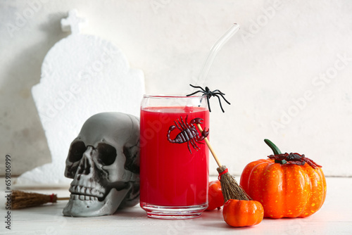 Glass of delicious red cocktail, skull and pumpkins for Halloween celebration on light background © Pixel-Shot