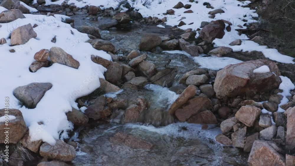 Close view of water running down in a creek surrounded by snow in the Granite Hills.