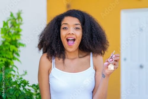 Young African American woman holding home keys at outdoors with surprise and shocked facial expression