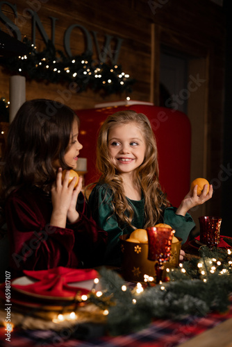 two girlfriends are sitting in the kitchen at the table with oranges in their hands, waiting for Christmas