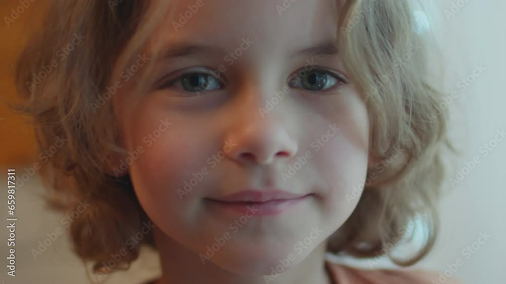 Close-up portrait of Caucasian boy standing calmly indoors wearing orange shirt looking at window and at camera with smile Close-up portrait of Caucasian boy standing calmly indoors wearing orange shirt looking at window and at camera with smile