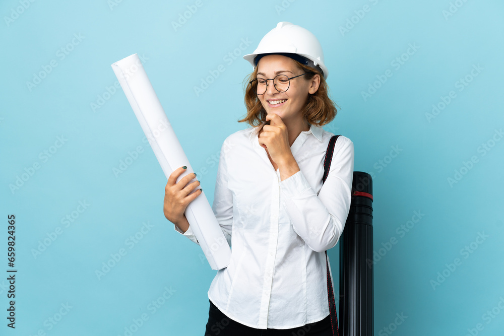 Young architect Georgian woman with helmet and holding blueprints over isolated background looking to the side and smiling Young architect Georgian woman with helmet and holding blueprints over isolated background looking to the side and smiling