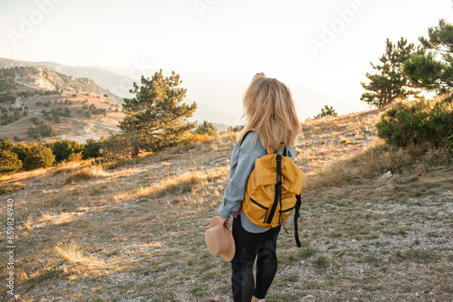 Back view of the plus size woman walks in the mountain. The gil admires beautiful views of landscape. Travel and tourism. Hiking. The overweight woman holding yellow bagpack photo