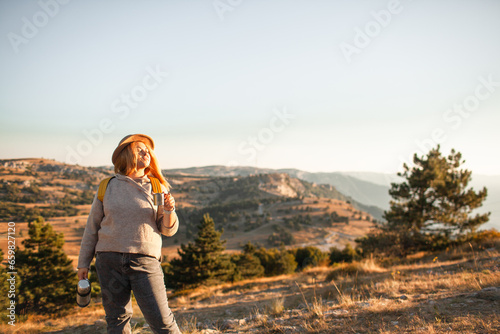 The plus size woman walks in the mountain. The gil admires beautiful views of landscape. Travel and tourism. Hiking. The overweight woman holding yellow bagpack