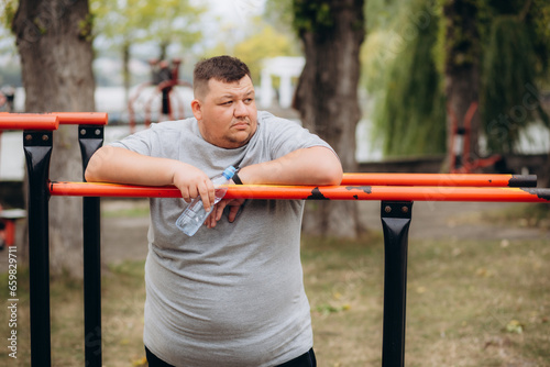 Picture of fat man looks tired while drinking a bottle of water after exercising in the park