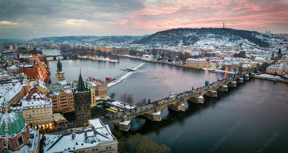 Panoramic view of the snow covered cityscape of Prague, Czech Republic, with Charles Bridge and the old town during winter sunset time - obrazy, fototapety, plakaty 