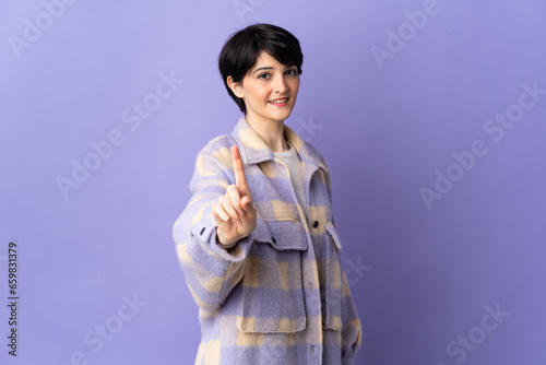 Woman with short hair isolated on purple background showing and lifting a finger