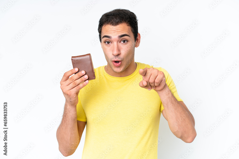 Young caucasian man holding a wallet isolated on white background surprised and pointing front Young caucasian man holding a wallet isolated on white background surprised and pointing front