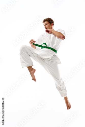 Athletic young man, karate, taekwondo sportsman in white kimono in motion, training isolated on white studio background. Concept of martial arts, combat sport, energy, strength, health. Ad