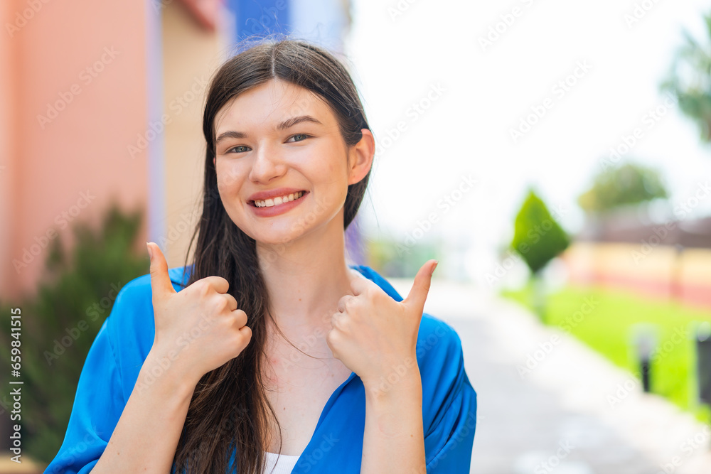 Young pretty woman at outdoors with thumbs up gesture and smiling