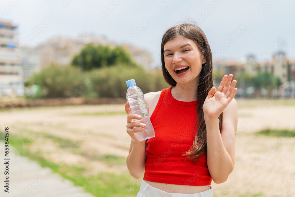 Young pretty Ukrainian woman with a bottle of water at outdoors saluting with hand with happy expression Young pretty Ukrainian woman with a bottle of water at outdoors saluting with hand with happy expression