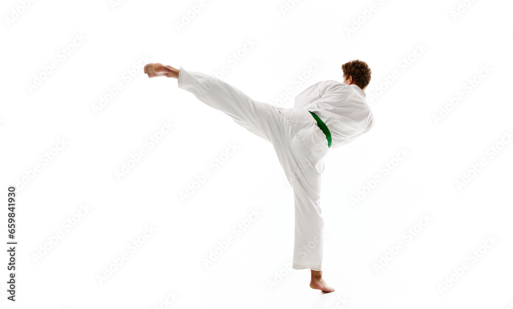 Side view of young man, karate, taekwondo athlete in kimono and green belt training isolated on white studio background. Concept of martial arts, combat sport, energy, strength, health. Ad