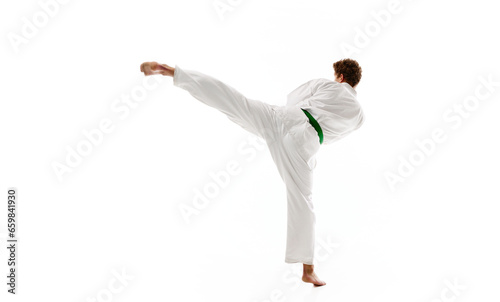Side view of young man, karate, taekwondo athlete in kimono and green belt training isolated on white studio background. Concept of martial arts, combat sport, energy, strength, health. Ad