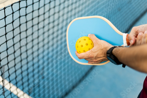 A close-up of a hand of an athlete with a pickleball racket and a ball about to make a serve. Pickle ball concept. Sports that are played with rackets.