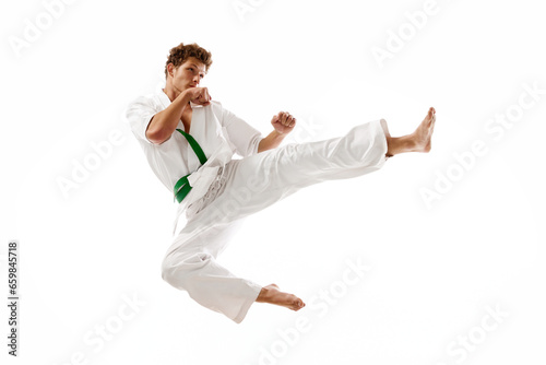 Kick in a jump. Young athletic man, karateka in motion training, practicing isolated on white studio background. Concept of martial arts, combat sport, energy, strength, health. Ad